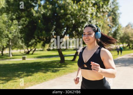 A young woman running around the park, happy, while listening to music with headphones, Zaragoza, Spain Stock Photo