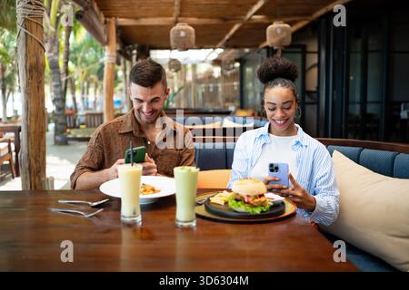 Young couple sharing dining experience at tropical restaurant, engaging with their online followers Stock Photo