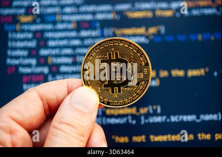Hand holding a Bitcoin coin in front of computer code representing cryptocurrency development Stock Photo