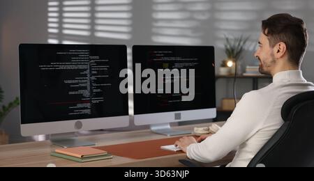 Programmer working on computer with dual monitors at table in office Stock Photo