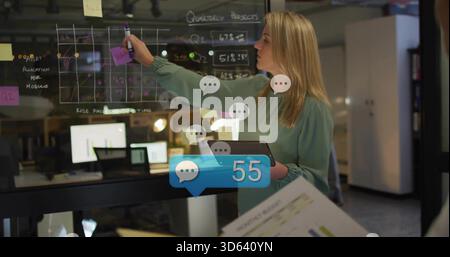 Writing manager in green blouse drawing grid on glass at office with tablet, monitors, copy space Stock Photo