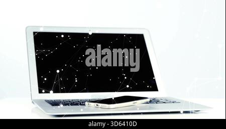 Displaying silver laptop with smartphone resting on keyboard at white desk, showing network overlay Stock Photo