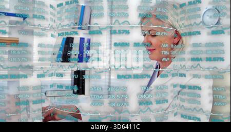 Reviewing woman in white lab coat reading papers at clinic desk, cyan financial overlay Stock Photo