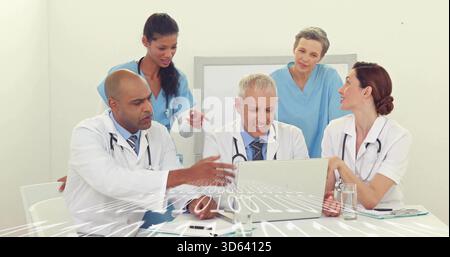 Discussing clinic team wearing lab coats and scrubs viewing laptop with binary code in meeting room Stock Photo