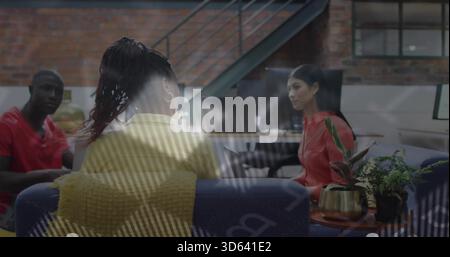 Discussing colleagues wearing yellow sweater and red tops on blue sofa in office, glass reflections Stock Photo