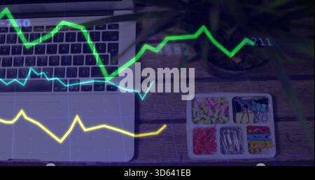 Displaying partial laptop keyboard, trackpad on left wooden desk with tray, plant, graph overlay Stock Photo