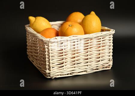 Fresh, vibrant oranges and lemons in a white basket on black. High-contrast still life ideal for health, food, and minimalist themes. Stock Photo