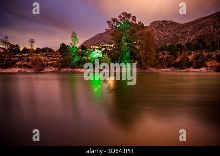 A dynamic night photograph of the Amadorio Reservoir, combining long exposure with light painting. Streaks of vibrant green light trace patterns throu Stock Photo