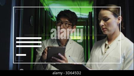 Holding tablet, techs wearing lab coats checking server racks and noting clipboard in data center Stock Photo