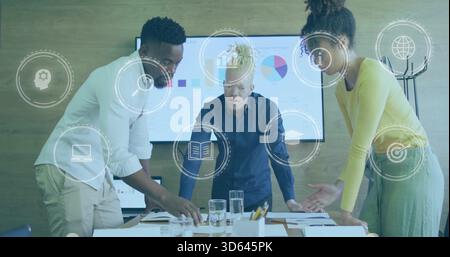 Leaning three person team reviewing charts at table in office wear, with monitor, reports, overlays Stock Photo