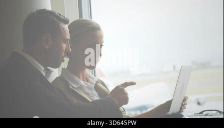 Leaning two professionals in blazers working over laptop at airport gate, window showing airplane Stock Photo