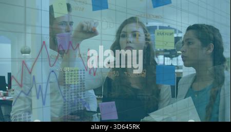 Writing woman in dark top drawing graphs on glass whiteboard at open office with sticky notes Stock Photo