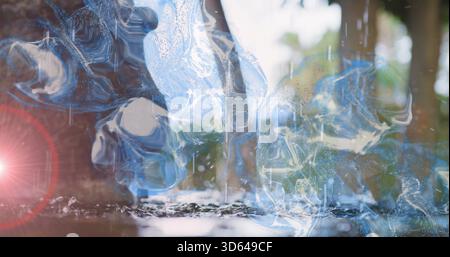 Floating glassy blue water swirls creating reflections on shallow pool near trees with lens flare Stock Photo