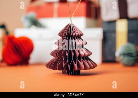 Paper Christmas decoration on blurred background of colorful gift boxes and Christmas tree balls, close-up. Stock Photo