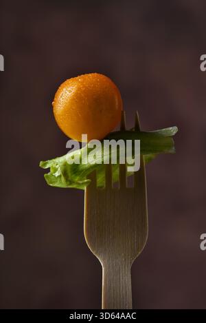 A yellow cherry tomato stuck on a bamboo fork with a leaf of lettuce against a warm brown background. Stock Photo
