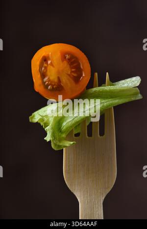 A yellow cherry tomato cut in half on a bamboo fork with a leaf of lettuce agaist a warm brown background. Stock Photo