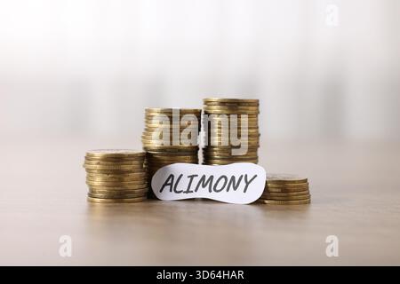 Paper note with word Alimony and stack of coins on wooden table, closeup Stock Photo