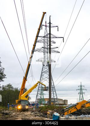 Electrical engineers and cranes assemble a high-voltage power transmission tower at an industrial site, showcasing energy infrastructure construction Stock Photo
