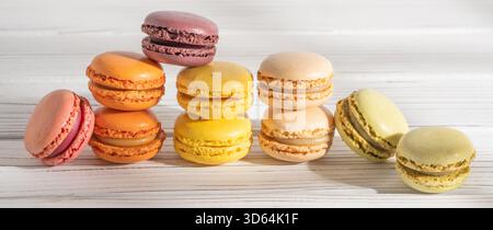 An array of colorful macarons is arranged in a row on a white wooden background, forming a gradient of hues. Stock Photo