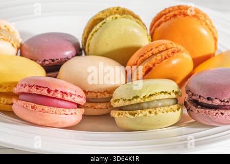 A collection of colorful macarons in various shades sits casually arranged on a white plate. Stock Photo