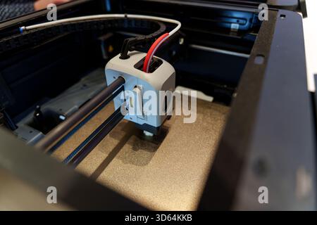 A close-up view of a 3D printer in action, showing the print head and rails, with wires attached, inside the machine's enclosure. High quality photo Stock Photo