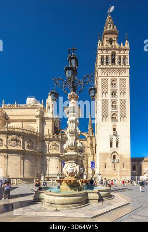 Seville, Spain - September 8, 2024: Seville Cathedral with The Giralda bell tower. Ornate fountain and historic tower in a sunny plaza. Tourists explo Stock Photo