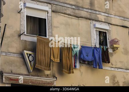 Lisbon, Portugal - 18 July 2020: View of clothes hanging from a window of an old building, casting shadows on the weathered facade. Stock Photo