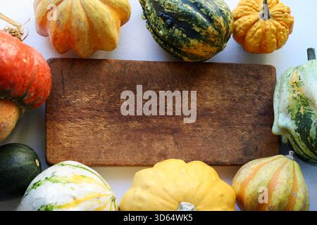 A wooden cutting board surrounded by various pumpkins on a white background. A rustic and seasonal backdrop, perfect for culinary or fall decorations. Stock Photo