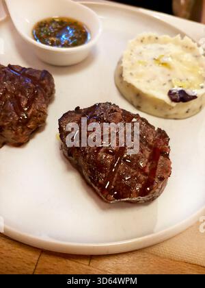 Grilled beef tenderloin, served with a sauce and a side of mashed potatoes on a white plate. Grilled beef medallions. Overhead view Stock Photo