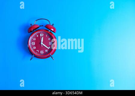 Red analog alarm clock on blue background highlights time awareness, urgency, and visual contrast in a minimalist composition. Stock Photo