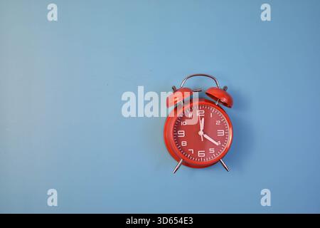 Red analog alarm clock on blue background highlights time awareness, urgency, and visual contrast in a minimalist composition. Stock Photo