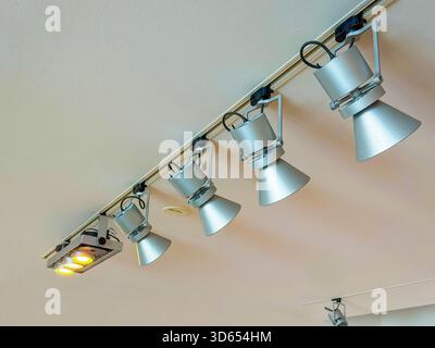 Modern ceiling-mounted track lighting system with multiple adjustable metal spotlights positioned in a row indoors Stock Photo