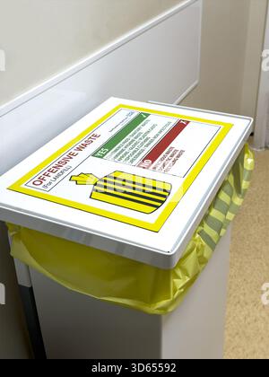 Medical waste bin with yellow bag and detailed disposal instructions for offensive waste in a hospital healthcare facility examination room Stock Photo