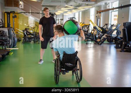 Disabled sportsman in wheelchair doing exercises with med ball on personal gym session with coach. Stock Photo