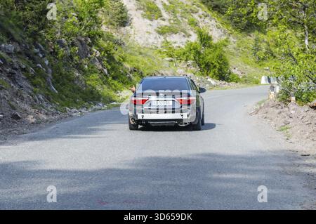 Black car driving on a winding road through the countryside, car without rear bumper, Georgia Stock Photo
