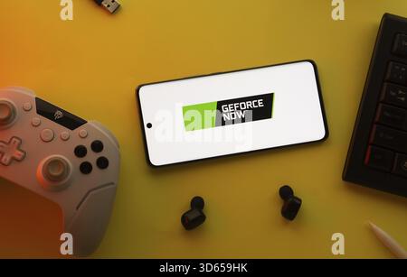 Dhaka, Bangladesh- 23 Mar 2025: Smartphone with Geforce Now logo, game controller, and earbuds on a yellow background Stock Photo