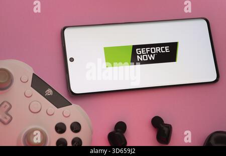Dhaka, Bangladesh- 22 Mar 2025: Smartphone with Geforce Now logo, game controller, and earbuds on a pink background Stock Photo