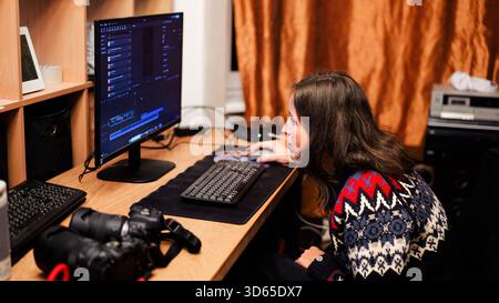 Focused woman working on video and photo editing at home office desk with computer monitor and professional cameras — modern remote work concept Stock Photo