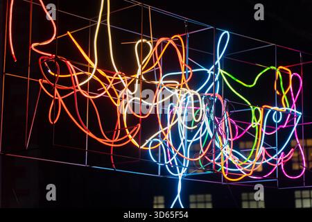 Colorful abstract neon light sculpture with tangled glowing tubes suspended inside geometric metal frame creating vivid illuminated artwork ideal for Stock Photo