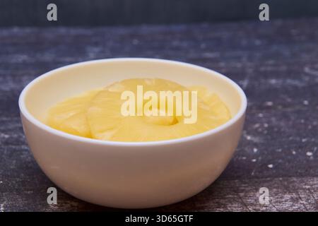 Sliced ​​pineapple, canned preserve. Close-up photograph with copy space on a table against a rustic background. Stock Photo