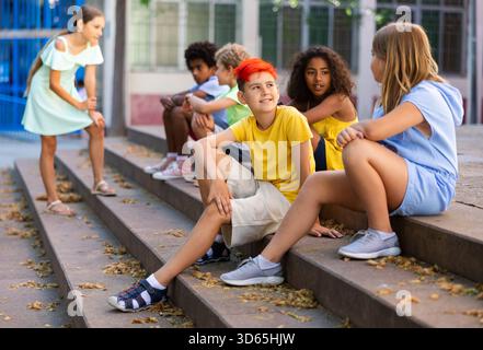 Happy tweenagers friends sitting on steps outdoors and chatting Stock Photo