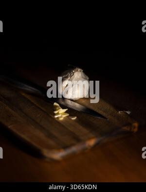 Close-up of a bulb of garlic on a wooden chopping board with a sliced clove of garlic Stock Photo