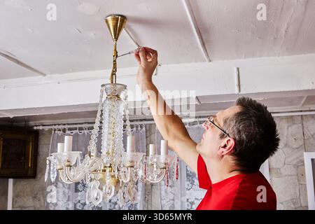 Uninstallation procedure captures technician taking down complete crystal chandelier from ceiling in countryside home, careful movement maintained. Stock Photo