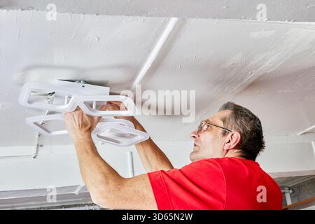 Fitting operation captures technician attaching new LED chandelier to ceiling in country home working with lighting unit during ceiling installation p Stock Photo