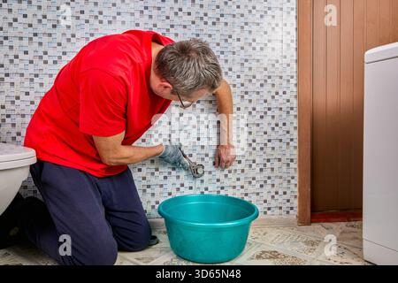 Plumber removes steel plug from water inlet pipe using special wrench and prepares connection point for washing machine installation. Stock Photo