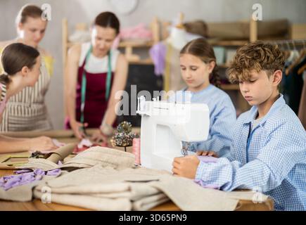 Preteen boy working at machine during group sewing course for kids Stock Photo