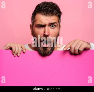 Surprised man pointing down at advertising board with empty space for text, mockup. Handsome male with blank signboard, advertising banner. Great offe Stock Photo