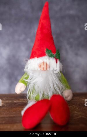 Christmas gnome with red hat resting on wooden base and dark background Stock Photo