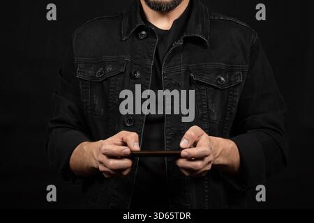 Close up to a man wearing a black denim jacket holding a smartphone in front of him Stock Photo