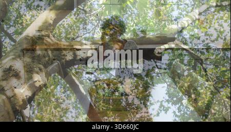 Sitting senior African American woman touching face at piano by window, with tree canopy overlay Stock Photo
